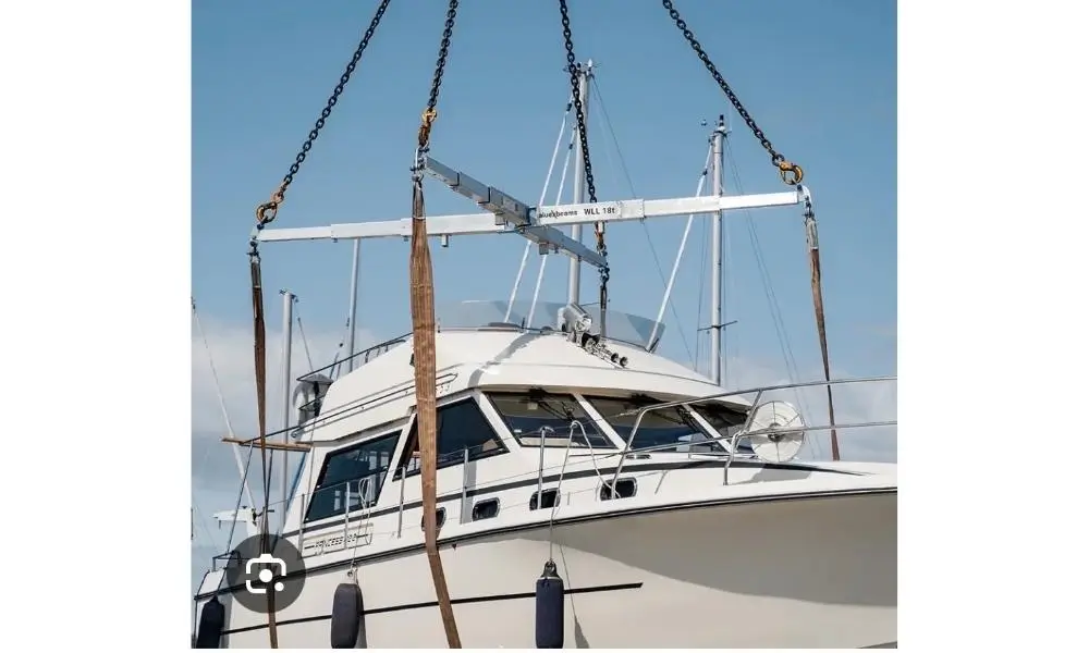 Bela motorjahta Princess 330 podignuta autodizalicom pomoću spreader beam ramena WLL 18 t, crnih lanaca i smeđih traka za podizanje pod trup — podizanje plovila u marini, mobilni kran i autodizalica 40 t Metal Pro